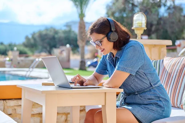 Ώριμη γυναίκα που εργάζεται σε εξωτερικούς χώρους με ακουστικά χρησιμοποιώντας φορητό υπολογιστή. — Φωτογραφία Αρχείου