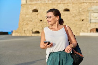 Gülümseyen orta yaşlı bir kadının açık hava portresi eski bir kasabada yürüyor.