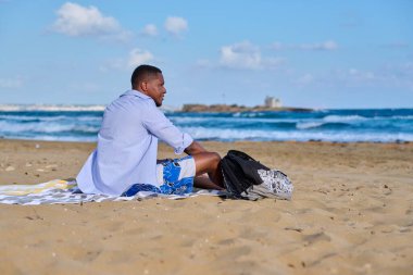 Genç, pozitif erkek turist sahilde dinleniyor.