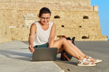 Laptop kullanan olgun bir kadın turist, eski Avrupa tarihi kalesi geçmişi.
