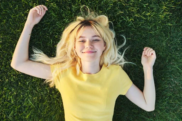 ท็อปวิวของสาวสวยวัยรุ่นผมบลอนด์นอนบนหญ้าสีเขียว . — ภาพถ่ายสต็อก