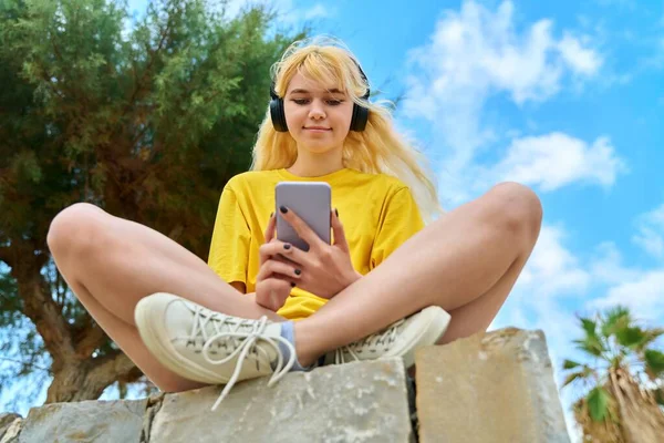 Dospívající dívka ve sluchátkách při pohledu do smartphonu — Stock fotografie