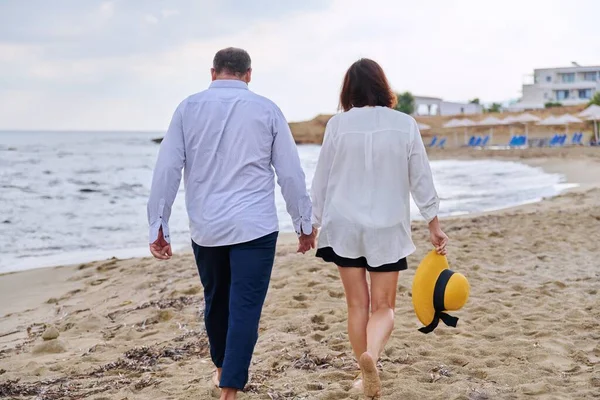 Happy middle aged couple walking together on the beach, back view — 图库照片