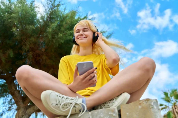 Дівчина-підліток в навушниках дивиться в смартфон — стокове фото