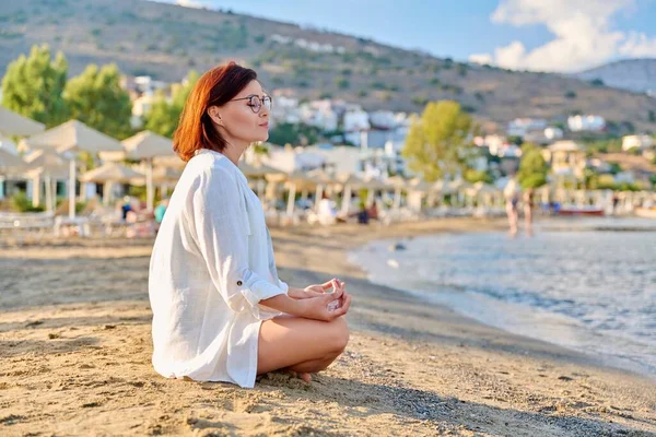 Mujer madura sentada en posición de loto meditando en la playa. — Foto de Stock