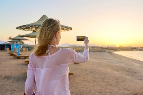 Vrouw maakt foto op smartphone van oranje zonsondergang op zee — Stockfoto