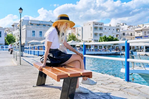Дівчина-підліток в капелюсі відпочиває, сидить, чекає в літньому морському місті — стокове фото