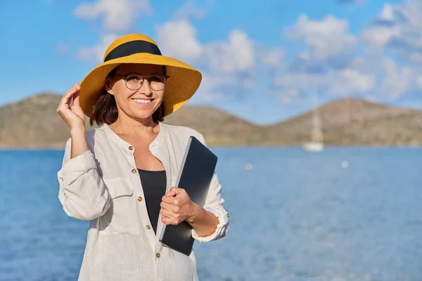 바닷가에 랩탑 이 있는 모자를 쓴 행복 한 성숙 한 여성의 모습, 복사 공간 — 스톡 사진