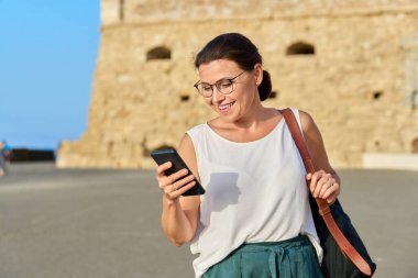 Elinde akıllı telefonla yürüyen bir kadın, eski şehirde sırt çantalı bir kadın.