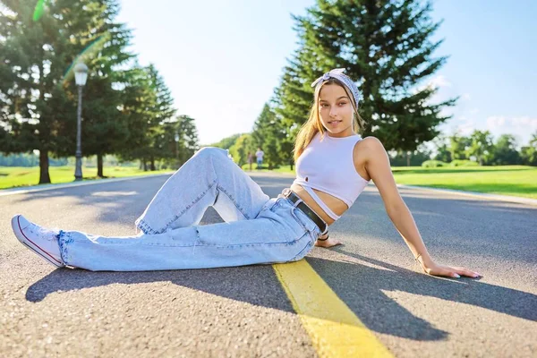 Модная девочка-подросток позирует сидя на дороге в парке. — стоковое фото