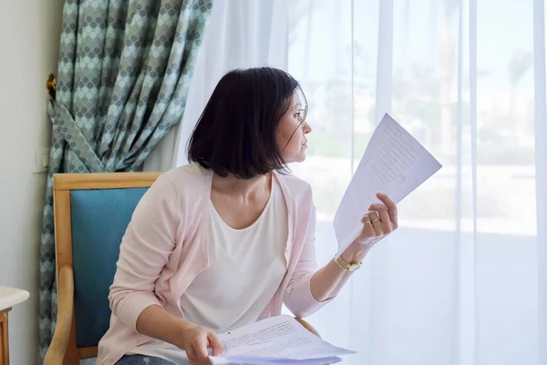 Ernsthafte reife Frau liest Papierdokumente zu Hause im Sessel. — Stockfoto