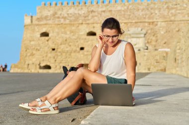 Laptop kullanan olgun bir kadın turist, eski Avrupa tarihi kalesi geçmişi.