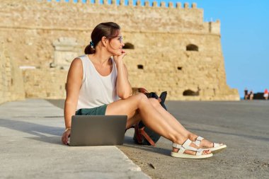 Laptop kullanan olgun bir kadın turist, eski Avrupa tarihi kalesi geçmişi.