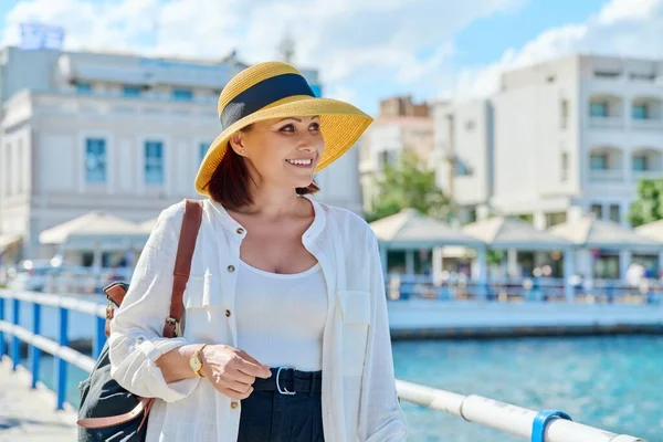 모자를 쓴 성숙 한 여자, 오래 된 관광 도시의 해변 산책로를 따라 걷고 있다 — 스톡 사진