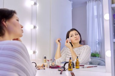 Orta yaşlı cilt bakımı yapan kadın Gua sha kazıyıcıyla yüz masajı yapıyor..