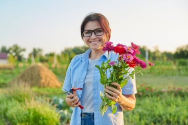 Gülümseyen orta yaşlı kadın bahçede bir buket taze zinnia çiçeği tutuyor.
