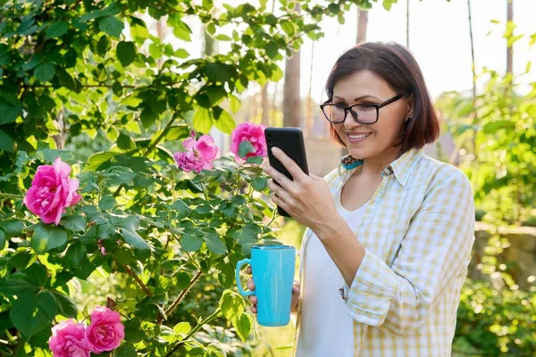 Ώριμη γυναίκα αναπαύεται στην πίσω αυλή χρησιμοποιώντας smartphone για βιντεοκλήση — Φωτογραφία Αρχείου