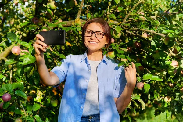 快乐的女人在花园里给树上成熟的苹果拍照. — 图库照片