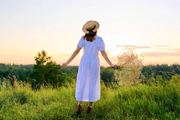 Pohled zezadu na romantickou ženu v bílých šatech se slaměným kloboukem při západu slunce — Stock fotografie