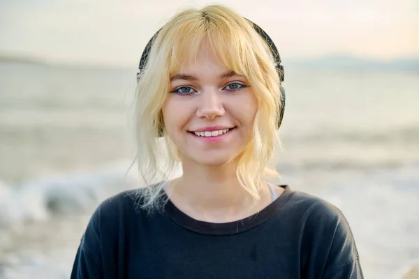 Portrét usměvavé dospívající ženy ve sluchátkách, na pláži, zblízka obličej, úsměv se zuby — Stock fotografie