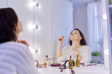 Orta yaşlı cilt bakımı yapan kadın Gua sha kazıyıcıyla yüz masajı yapıyor..