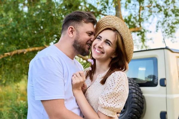 Feliz abrazo hombre y mujer cerca de coche, naturaleza de verano prado salvaje fondo —  Fotos de Stock