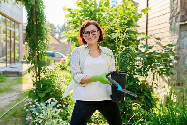 Glimlachende vrouw met bloempot met pioenplant en tuinschep — Stockfoto