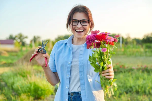 Улыбающаяся женщина средних лет держит букет свежих цветов зиннии в саду — стоковое фото