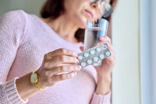 Ältere traurige Frau mit Pillen-Blase und einem Glas Wasser zu Hause. — Stockfoto