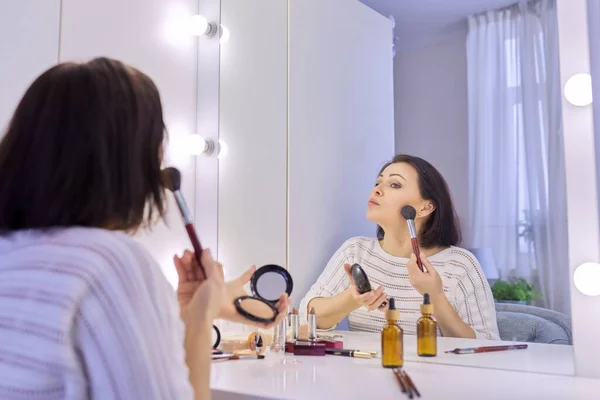 Mulher de meia-idade bonita fazendo maquiagem na frente de um espelho. — Fotografia de Stock