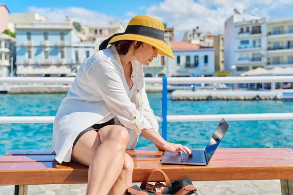 Зріла жінка в капелюсі з ноутбуком на морській набережній в місті . — стокове фото