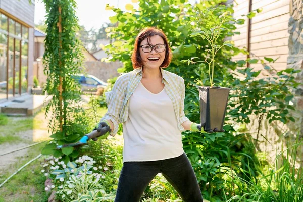 Wanita tersenyum dengan pot bunga dengan tanaman peony dan sekop taman — Stok Foto