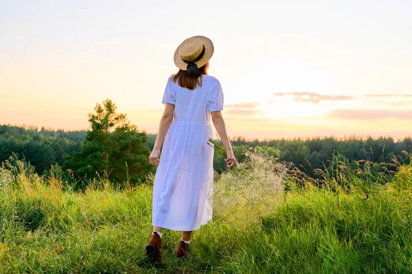 Pohled zezadu na romantickou ženu v bílých šatech se slaměným kloboukem při západu slunce — Stock fotografie