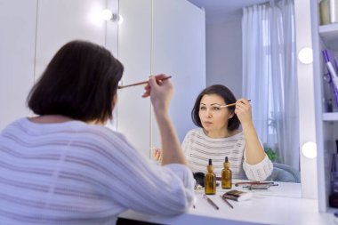 Güzel orta yaşlı kadın aynanın önünde makyaj yapıyor..