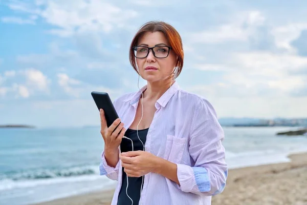 Μέση ηλικία θλιβερή σοβαρή γυναίκα σε ακουστικά με smartphone εξωτερική. — Φωτογραφία Αρχείου
