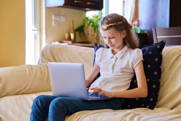 Bambino ragazza a casa sul divano con un computer portatile. — Foto Stock