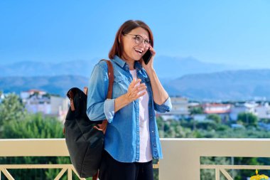 Orta yaşlı bir kadın dışarıda telefonla konuşuyor.