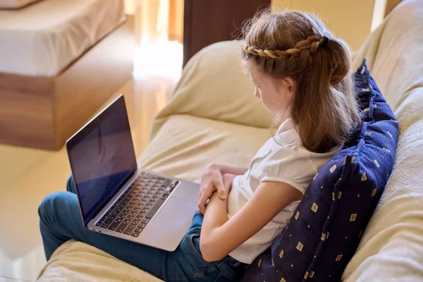 Bambino ragazza a casa sul divano con un computer portatile. — Foto Stock