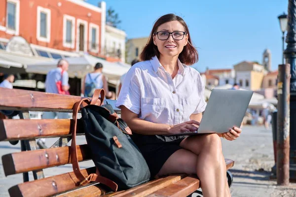 Жінка середнього віку сидить на лавці в місті, використовуючи ноутбук — стокове фото
