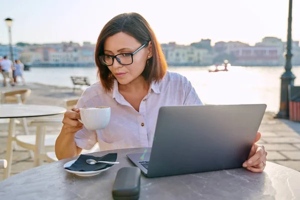 Σοβαρή μεσήλικη επιχειρηματίας σε υπαίθριο καφέ χρησιμοποιώντας φορητό υπολογιστή — Φωτογραφία Αρχείου