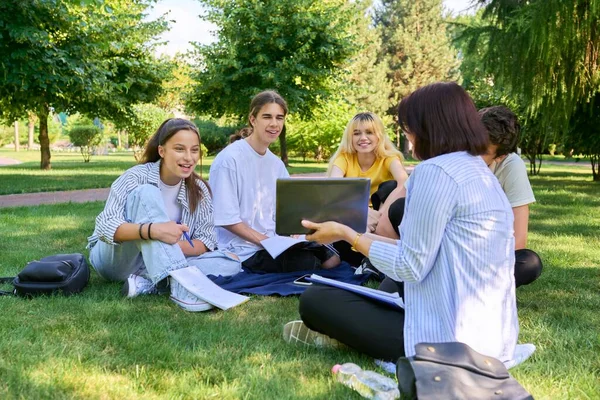 Al aire libre, grupo de estudiantes con profesora sentada en la hierba — Foto de Stock