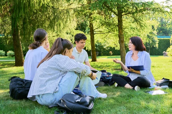 Al aire libre, grupo de estudiantes con profesora sentada en la hierba — Foto de Stock