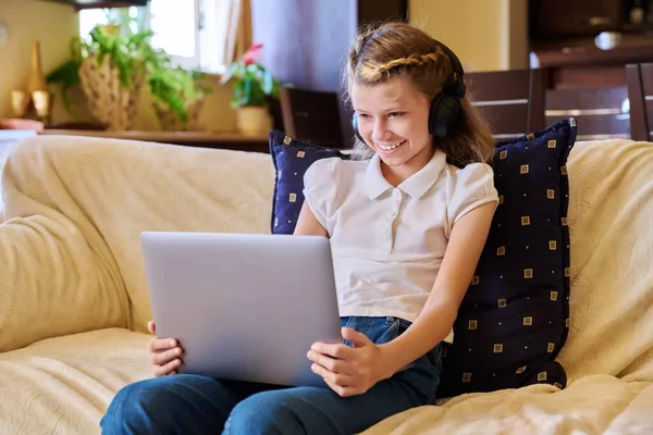 Girl child in headphones resting at home on sofa using laptop — Stock Photo, Image