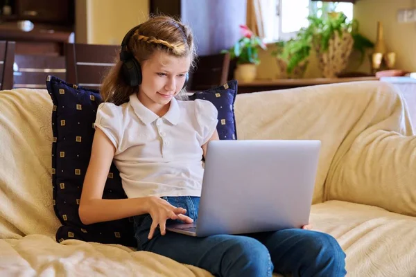 Ragazza bambino in cuffia a riposo a casa sul divano utilizzando il computer portatile — Foto Stock