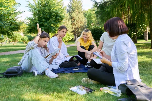 Outdoor, grupa uczniów z nauczycielką siedzącą na trawie — Zdjęcie stockowe