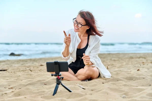 Középkorú nő ül a strandon okostelefonnal videohívás — Stock Fotó