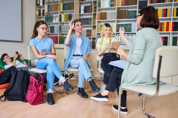 Grupp tonårsstudenter med kvinnlig lärare i biblioteket — Stockfoto