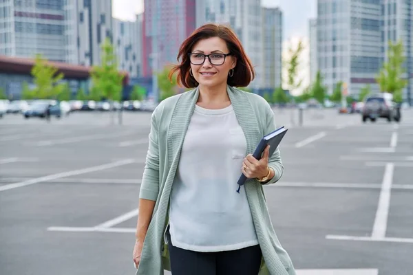 Sorrindo bem sucedido mulher de negócios maduro andando ao ar livre, moderno estilo urbano fundo. — Fotografia de Stock