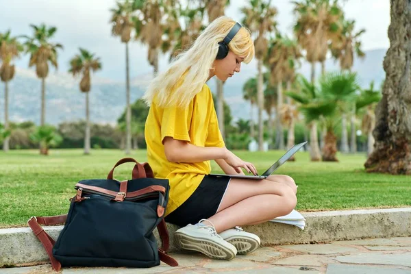 Žena dospívající student ve sluchátkách sedí v parku s notebookem. — Stock fotografie