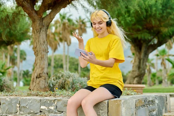 Hipster adolescente en los auriculares con teléfono inteligente hablando en el enlace de vídeo — Foto de Stock